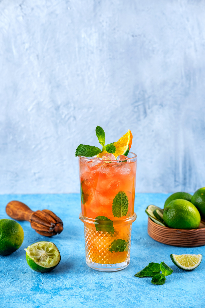 Strawberry Mojito. Cocktail with strawberries, mint, lime and ice in a glass on a blue background. Homemade beverage.